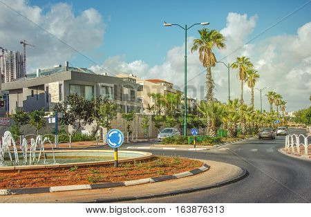 Rishon LeZion Israel-May 27 2016: Roundabout with small fountain on Heil HaTothanim Street. Tree private cars driving on the street with green palms. 2-story houses are seen in left site. This picture is taken in bright sunny day