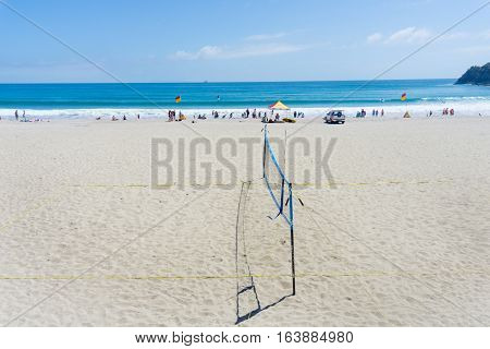 Mount Maunganui, New Zealand - December 21, 2016; ocean-beach with people enjoying summer and beach activities beyond beach volleyball net lifesavers flags and shelter.