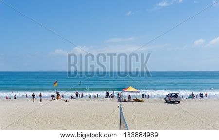 Mount Maunganui, New Zealand - December 21, 2016; ocean beach with beach volleyball net and people enjoying summer and beach activities between the flags and lifesavers shelter.