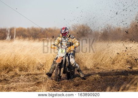 KHABAROVSK RUSSIA - OCTOBER 23 2016: Enduro bike rider on a field with dry grass in autumn. The motorcycle skids and makes a lot of mud splashes