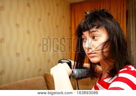 Girl dries hair and makes the hairstyle in her room. She uses the Hairdryer and comb. The home interior 2