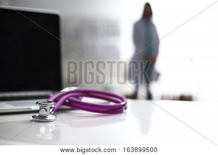 Laptop and stethoscope on the desk , doctors standing in the background.