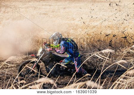 KHABAROVSK RUSSIA - OCTOBER 23 2016: Enduro bike rider on a field with dry grass in autumn. The motorcycle skids and makes a lot of mud splashes