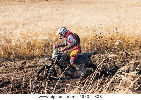 KHABAROVSK RUSSIA - OCTOBER 23 2016: Enduro bike rider on a field with dry grass in autumn. The motorcycle skids and makes a lot of mud splashes