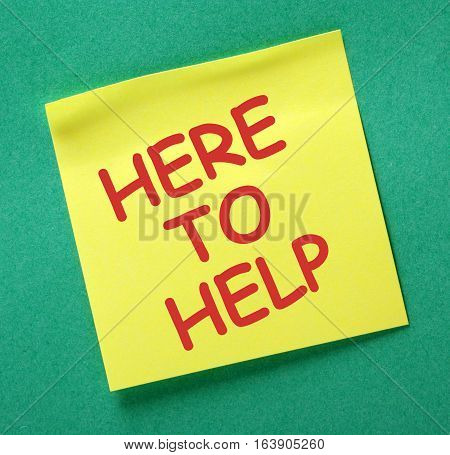 The words Here to Help on a yellow sticky note posted on a green noticeboard as a reminder