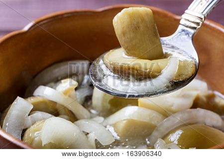 Spoon with marinaded mushroom and onion over pot with mushrooms. Close up photo.