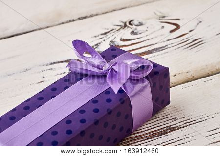 Bow on purple gift box. Present package on wooden plank. Aesthetic way of greeting.