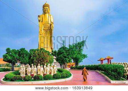 KAOSHIUNG, TAIWAN - NOVEMBER 24: View of a big gold buddha statue with a monk walking on the monastery ground on November 24, 2016 in Kaoshiung