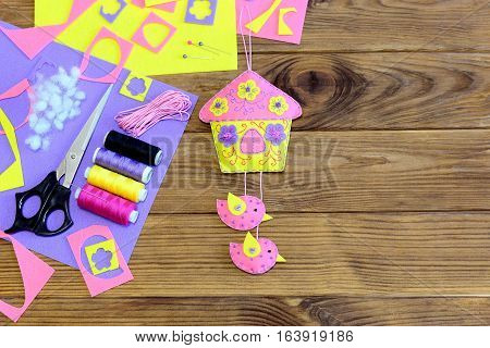 Wall decor made from felt. Bright hanging house with birds and flowers. Sewing materials and tools on wood background with copy space for text. Easter wall decor. Easy and beautiful DIY idea. Top view