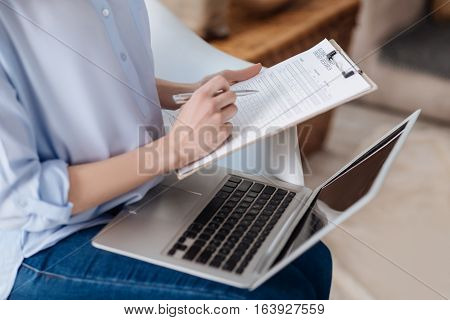 Be responsible. Close up of young delighted pregnant womans hands makig notes and holding documents while she working at home.