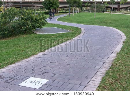 cycleway signposted a ground bikeway with two cyclists circling at background. Bike lane between trees in Jardin del Turia in Valencia Spain