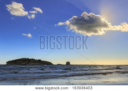 Gargano coast: Portonuovo beach,Vieste-(Apulia) ITALY-Islet between waves dominated by cloud crossed by sunbeams.