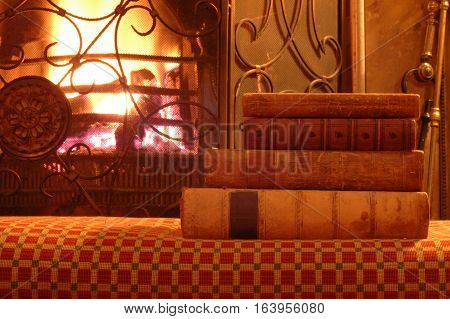 A pile of old books sitting by an warm fire.