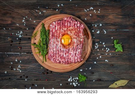 Homemade raw minced meat with egg and herbs closeup top view.