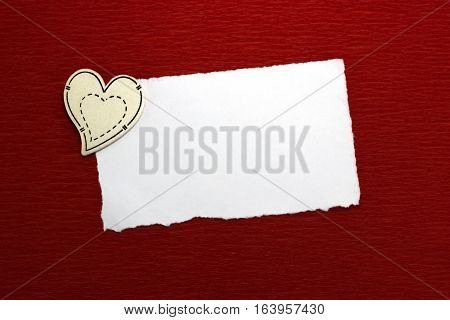 Wooden heart and white sheet of paper on a red background