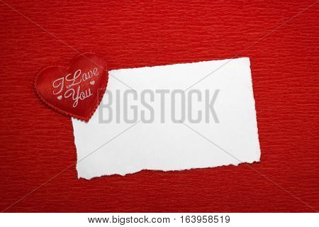 Red heart with an inscription and a white sheet of paper on a red background