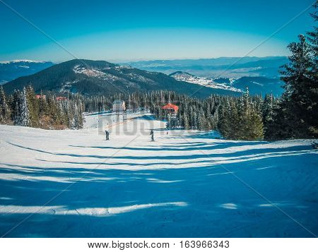 Skiers on the ski resort on a background of snow-capped mountain peaks blue sky and green trees