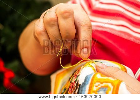 The cross stitching. Photo of woman hands closeup, which holds the needle and the embroidering.