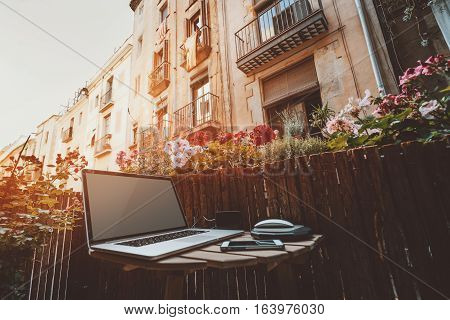 Small cozy beautiful workspace on balcony with laptop on wooden table mouse smartphone and a lot of flowers around on sunny summer day facades behind of historical district of Barcelona - El Born