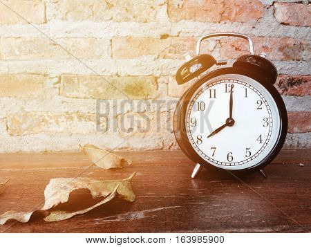 Retro black alarm clock with eight o'clock and dry leaves on wooden table and brick wall background