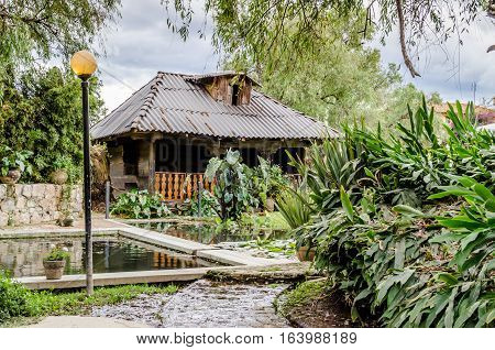 Horizontal photo in color of an abandoned cottage in the middle of a garden and an artificial pond