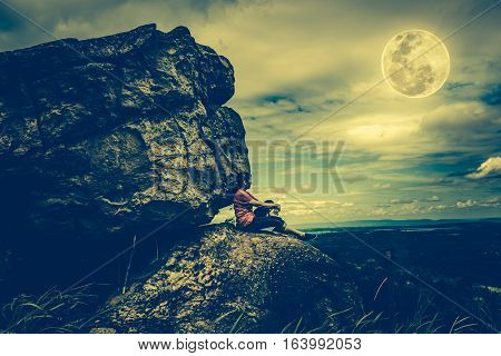 Woman Sitting On Boulders, Sky With Cloudy And Full Moon. Low Key And High Contrast Style.