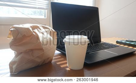 A Businessmans Desk With A Disposable Cup For Coffee And Fast Food. Open Laptop Computer. Breakfast 