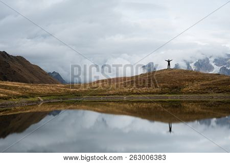 Koruldi lake with a mirror reflection of clouds. View of the Caucasus Mountains. Hiker stands on top of the hill. Samegrelo-zemo svaneti, Georgia