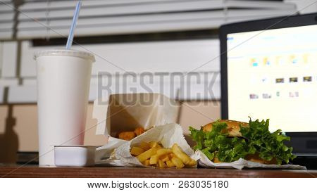 A Businessmans Table With A Disposable Cup For Coffee And Fast Food. Open A Laptop. Late Dinner At T