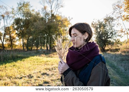 Young Woman With A Bunch Of Field Grasses Enjoying Beautiful Late Summer Day. Portrait Of Female Wit