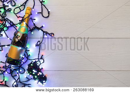 Christmas Background With Champagne And Luminous Colourful Garland On Wooden Background, Copy Space
