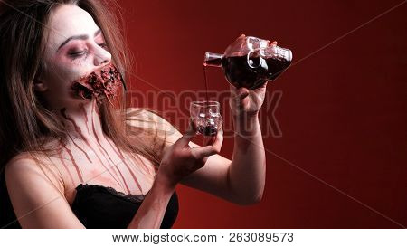 Halloween Party. A Girl With A Mouth Sewn Up And Bloody Smudges Around Her Neck Pours Blood Or Wine 
