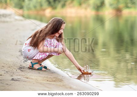girl playing with a toy sailing ship by the river