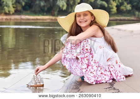girl playing with a toy sailing ship by the river