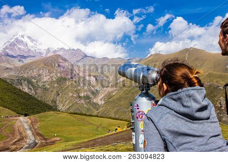 Woman And Man Looking In Binoscope Directed Towards The Snowy Mountain Tops Of Kazbeg From The View 