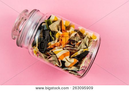 Colored Pasta In Glass Jar On Pink Background.