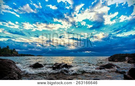 Confetti Sky Lakeshore. Colorful Clouds Fill The Atmosphere Above A Rocky Lake Superior Shoreline. S