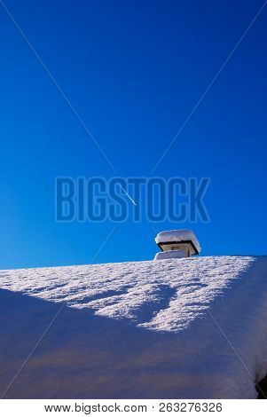 Roof With Fireplace Covered From High Layer Of Snow In Contrast With Blue Sky
