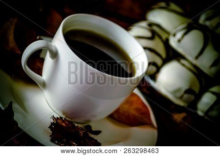 White Cup And Saucer With Tea Or Coffee Is On The Table, Autumn Orange Leaves, Next To It Is A Plate