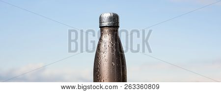Thermo Stainless Bottle, Sprayed With Water. Sky And Forest On Background. Thermos Of Maro Color.