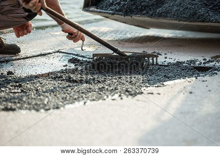 Closeup View Of Worker Using Rakes To Arrange Fresh Asphalt On The Road That Is Being Repaired.