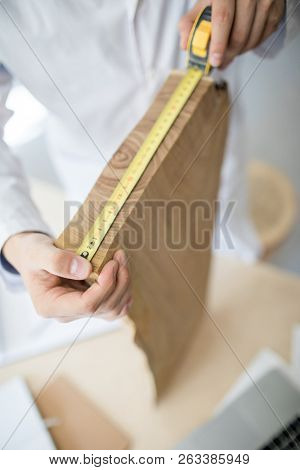 Young carpenter measuring width of wooden board with yellow tape at work