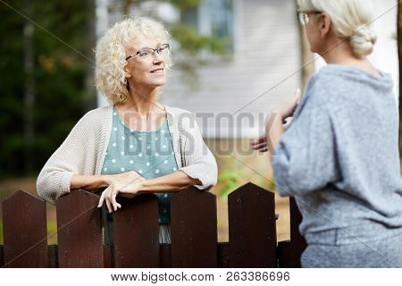 Two mature female neighbours talking through fence about everyday life stuff
