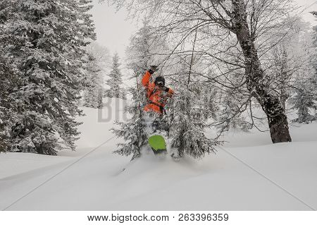 Male Snowboarder Jumping Between Trees On The Powdered Snow In The Mountain Tourist Resort In Goderz