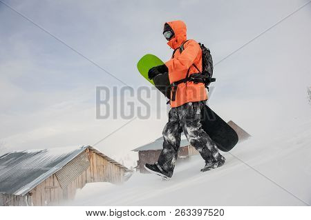 Man Walking With The Snowboard In Hands Down The Slope In The Mountain In The Popular Tourist Resort