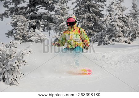 Girl Running Down The Mountain Slope On The Snowboard On The Background Of Sky And Trees In The Moun