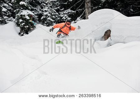 Man Jumping From The Mountain Slope On The Snowboard On The Background Of Trees In The Mountain Tour