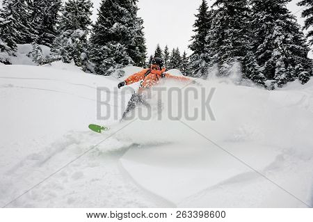 Male Snowboarder Running Down The Mountain Hill On The Snowboard On The Background Of Sky And Trees 