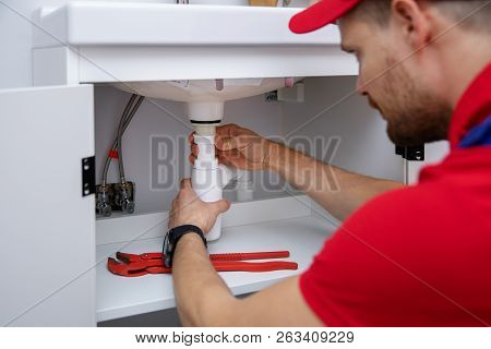 Plumber Installing Sink Siphon In Domestic Bathroom