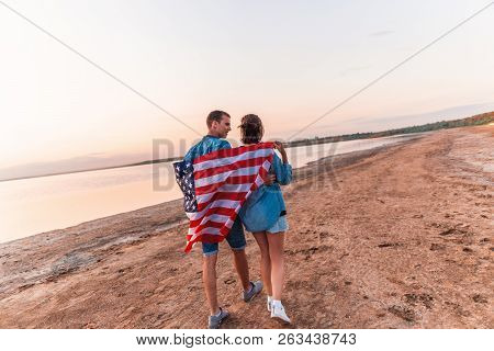 American Couple Covered In American Flag Walking On Beach